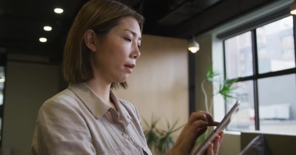 Mujer de negocios asiática de pie usando tableta digital en una oficina moderna — Vídeos de Stock