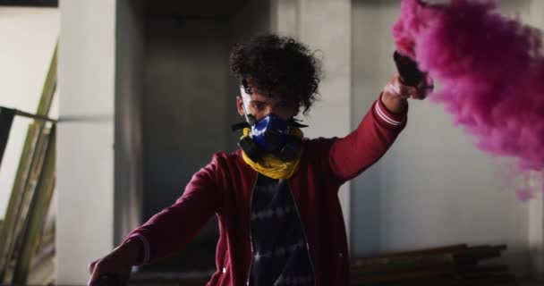 Mixed race man holding blue and purple flares standing in an empty building — Stock Video