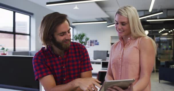 Personas de negocios caucásicos utilizando tableta digital hablando y sonriendo en la oficina moderna — Vídeos de Stock