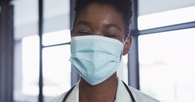 Yüz maskesi takmış, kameraya bakan Afro-Amerikan kadın doktor portresi.