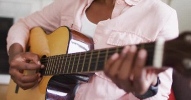 Evde gitar çalan Afrikalı Amerikalı kadının orta bölümü.