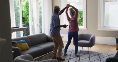 Karışık ırk son sınıf çifti evdeki oturma odasında dans ediyor.