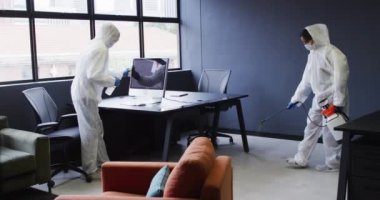 Koruyucu giysiler giyen temizlikçiler modern ofis alanını sterilize ediyorlar. İş yerinde hijyen, covid 19 koronavirüs salgını sırasında..