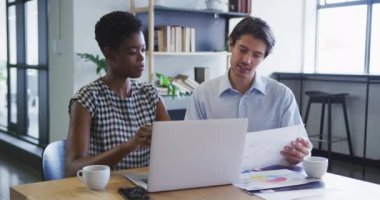Çeşitli iş arkadaşları masa başında dizüstü bilgisayarlarını kullanarak ofisteki evrak işlerini hallediyorlar.