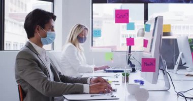 Ofisteki maske takan ve aralarında hijyen ekranı olan çeşitli iş arkadaşları. İş yerinde hijyen, covid 19 koronavirüs salgını sırasında sosyal mesafeler..