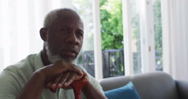 Evdeki kanepede otururken elinde baston tutan Afrikalı Amerikalı bir adam.