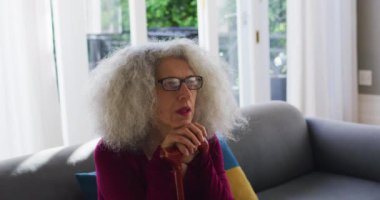 Evdeki kanepede otururken elinde baston tutan son sınıf beyaz kadın.