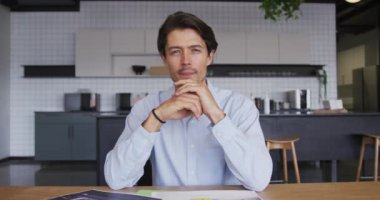 Kafkasyalı işadamı iş yerindeki mutfakta kameraya bakarak görüntülü konuşma yapıyor.