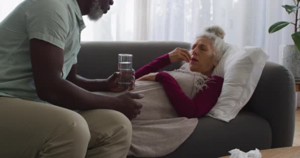 Αφροαμερικάνος που δίνει φάρμακα στην άρρωστη γυναίκα του στο σαλόνι στο σπίτι. — Αρχείο Βίντεο