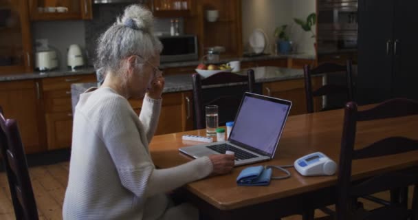 Mujer mayor caucásica sosteniendo medicamentos vacíos mientras recibe una videollamada en la computadora portátil en casa — Vídeos de Stock