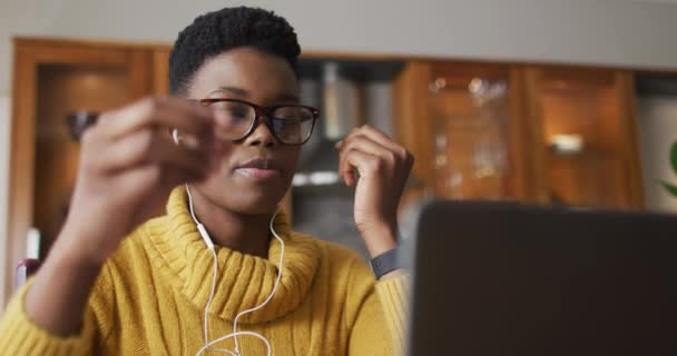 Afrikansk amerikansk kvinde iført øretelefoner ved hjælp af bærbar computer, mens du arbejder hjemmefra – Stock-video