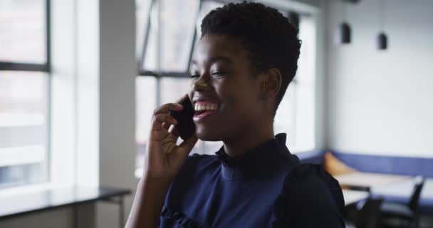 Uśmiechnięta mieszana bizneswoman wyścig stoi rozmawiając na smartfonie w biurze — Wideo stockowe