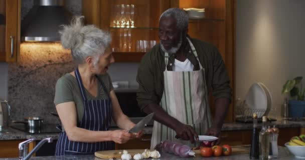 Enfermo de raza mixta pareja de ancianos con delantales picando verduras juntos en la cocina en casa — Vídeos de Stock