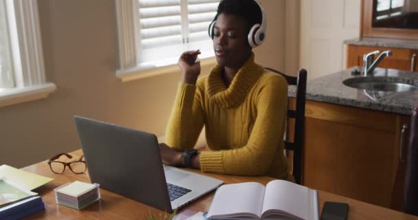 Африканская американка носит наушники с помощью ноутбука во время работы из дома — стоковое видео