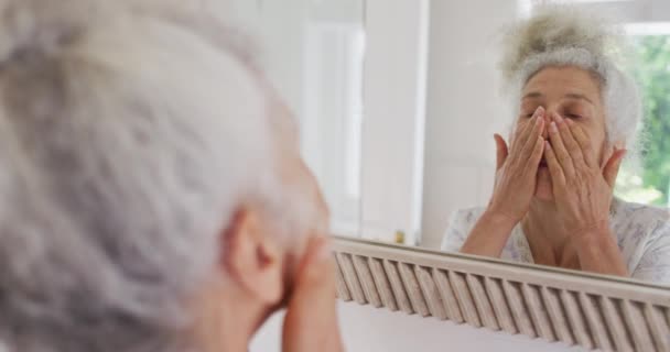 Donna anziana caucasica che si tocca il viso mentre si guarda allo specchio a casa — Video Stock