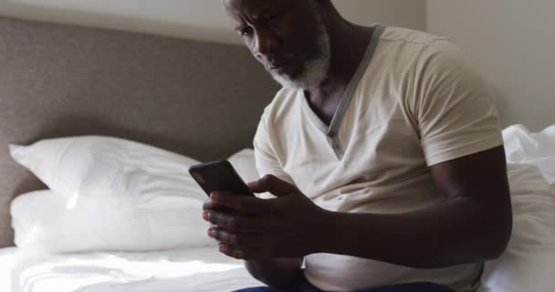 Homme âgé afro-américain utilisant un smartphone tout en étant assis sur le lit à la maison — Video