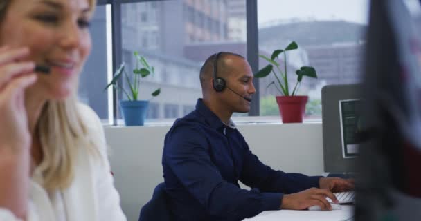 Çeşitli iş adamları bilgisayar kullanarak oturup telefon kulaklıklarıyla konuşuyorlar. — Stok video