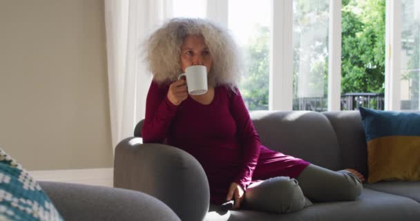 Senior caucásico mujer bebiendo café mientras viendo la televisión en casa — Vídeos de Stock