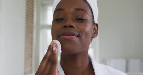 Ritratto di donna afroamericana in accappatoio che si pulisce la pelle con un batuffolo di cotone mentre guarda dentro — Video Stock