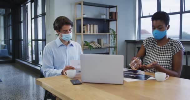 Diversos colegas de negócios usando máscaras faciais sentados usando laptop passando por papelada no escritório — Vídeo de Stock