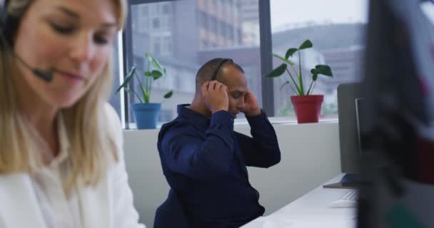 Çeşitli iş adamları bilgisayar kullanarak oturup telefon kulaklıklarıyla konuşuyorlar. — Stok video