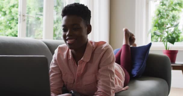 Wanita Afrika Amerika menggunakan laptop saat berbaring di sofa di rumah — Stok Video