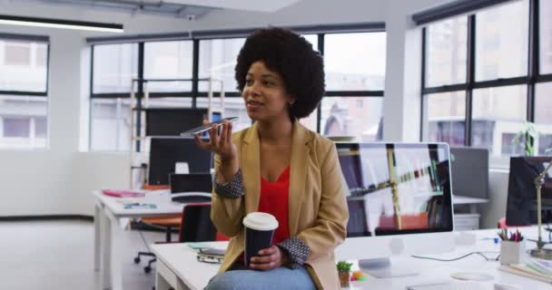 Femme d'affaires mixte assis sur le bureau tenant café parler sur smartphone dans le bureau — Video