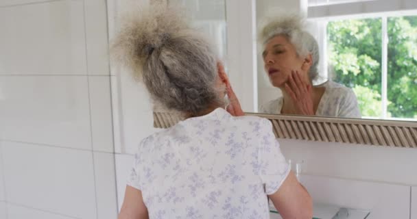 Donna anziana caucasica che si tocca il viso mentre si guarda allo specchio a casa — Video Stock