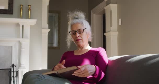 Senior caucasian woman reading a book while sitting on the couch at home — Stock Video