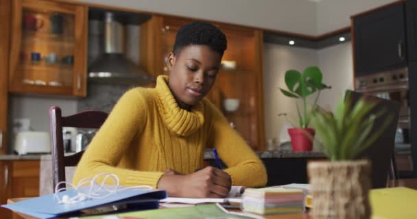 Mujer afroamericana tomando notas mientras trabaja desde casa — Vídeos de Stock