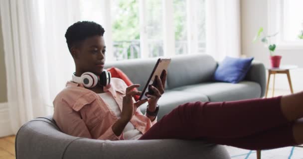 Африканская американка использует цифровой планшет, сидя дома на диване — стоковое видео
