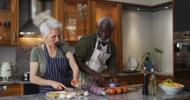 Hasta melez yaşlı çift önlük giyip evdeki mutfakta birlikte sebze doğruyorlar. — Stok video