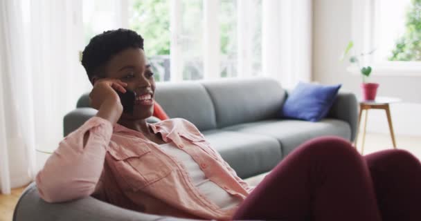 Африканская американка разговаривает по смартфону, сидя дома на диване — стоковое видео