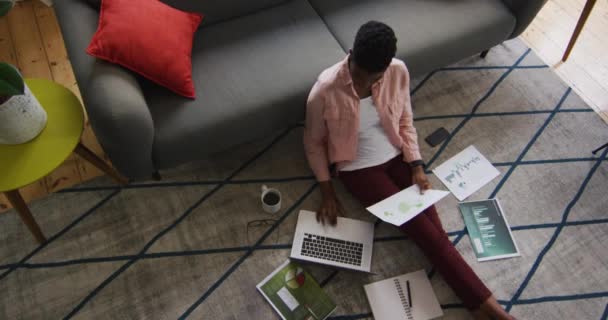 African american woman holding a document and using laptop while working from home — Stock Video