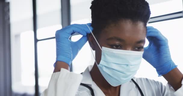 Портрет африканской женщины-врача в хирургических перчатках, надевающей маску для лица — стоковое видео