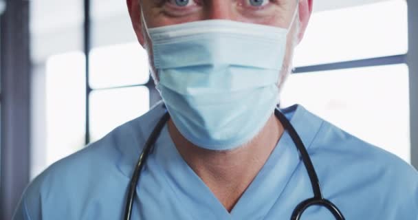 顔のマスクをした白人男性医師の肖像がカメラを見ている コロナウイルス中の医療従事者の衛生状態 Covid 19パンデミック — ストック動画