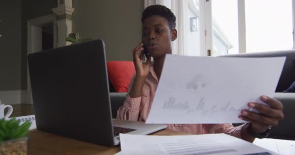African american woman holding a document talking on smartphone while working from home — Stock Video