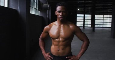 Gömleksiz Afrikalı Amerikalı adam boş bir şehir binasında kaslarını esnetiyor.