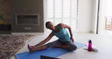 Karışık ırktan bir kadın laptopla paspasla antrenman yapıyor.