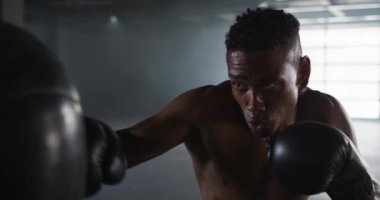 Afrikalı Amerikalı boks eldiveni giymiş boş bir binada kum torbası yumrukluyor.