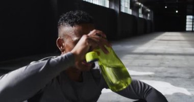 Afrikalı Amerikalı bir adam boş bir binada oturuyor ve kafasına su döküyor.