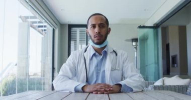 Video görüşmesi sırasında maskeli melez erkek doktor konuşuyor.