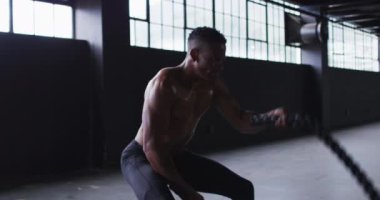 Gömleksiz Afro-Amerikan bir adam boş bir şehir binasında savaş halatları kullanıyor.