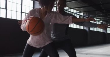 Afrika kökenli Amerikalı kadın ve erkek boş bir binada durup basketbol oynuyorlar.