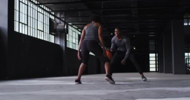 Afrika kökenli Amerikalı kadın ve erkek boş bir binada durup basketbol oynuyorlar.