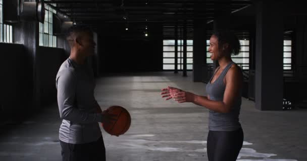 Afrykański Amerykanin mężczyzna i kobieta stojący w pustym budynku bawiący się koszykówką — Wideo stockowe
