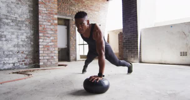 Afroamerikansk man tränar gör armhävningar på medicinboll i en tom stadsbyggnad — Stockvideo