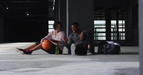 Afrikansk amerikansk man och kvinna vilar efter spelet dricksvatten och skrattar — Stockvideo