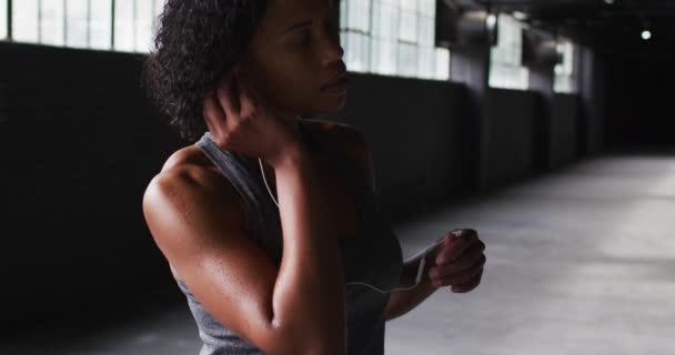 Potret wanita Afrika-Amerika yang berdiri di gedung kosong, meletakkan earphone di — Stok Video