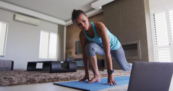 Mujer de raza mixta haciendo ejercicio en una alfombra con portátil — Vídeos de Stock